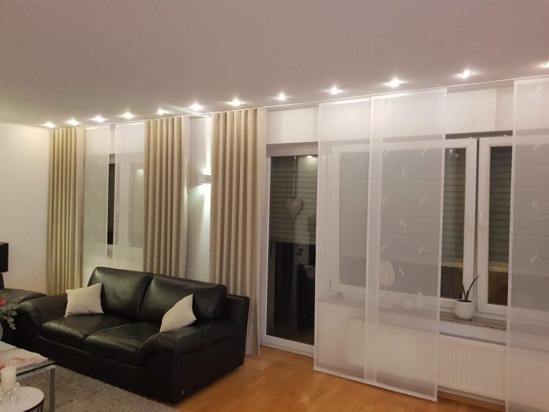 Wohnzimmer mit bodentiefen Gardinen und Schiebegardinen als Sicht- und Lichtschutz von M-Gardinendesign.