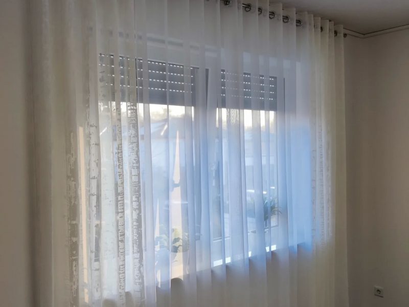 Fenster mit transparenter Gardine und dekorativem Seitenschal von M-Gardindendesign.