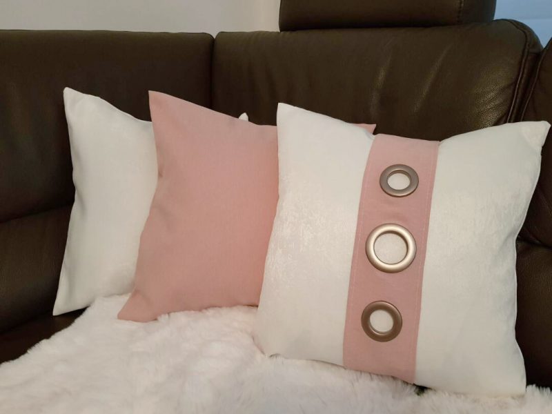 Weiße und rosafarbene Kissenbezüge nach Maß von M-Gardindendesign auf einem Bett arrangiert.