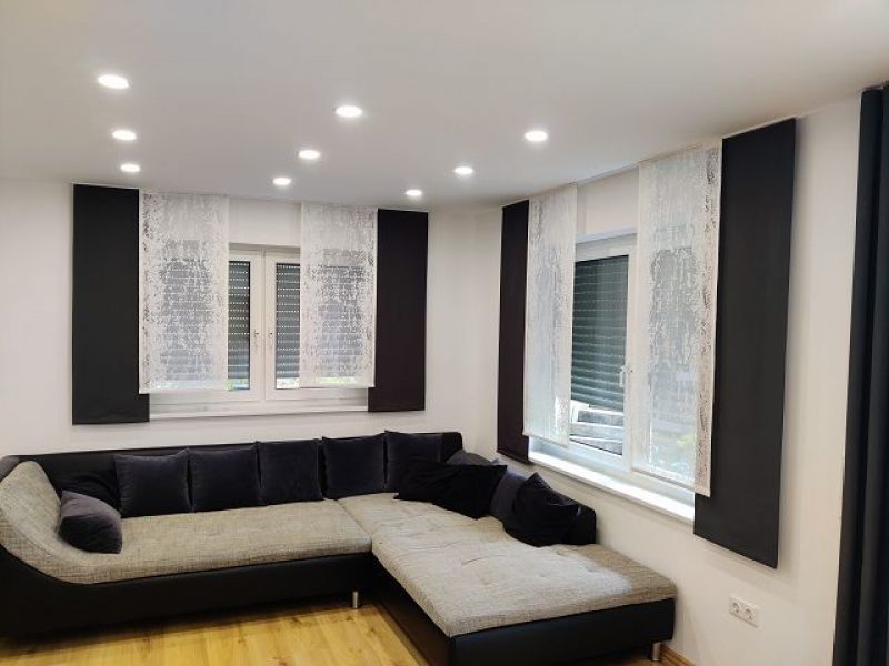 Modernes Wohnzimmer mit bodentiefen Fenstern und dunklen Vorhängen von M-Gardindendesign für optimalen Sicht- und Lichtschutz.