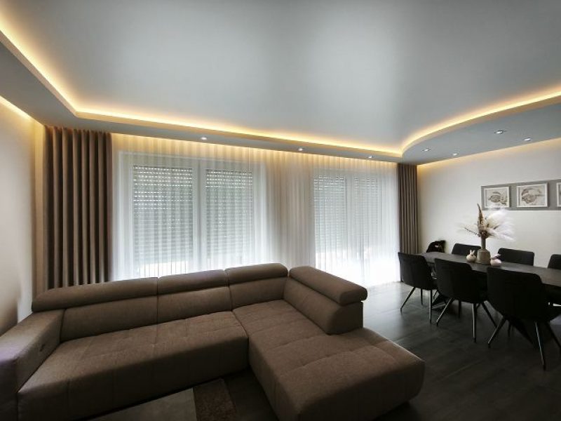 Modernes Wohnzimmer mit maßgefertigten Gardinen und indirekter Beleuchtung von M-Gardinendesign in Paderborn.